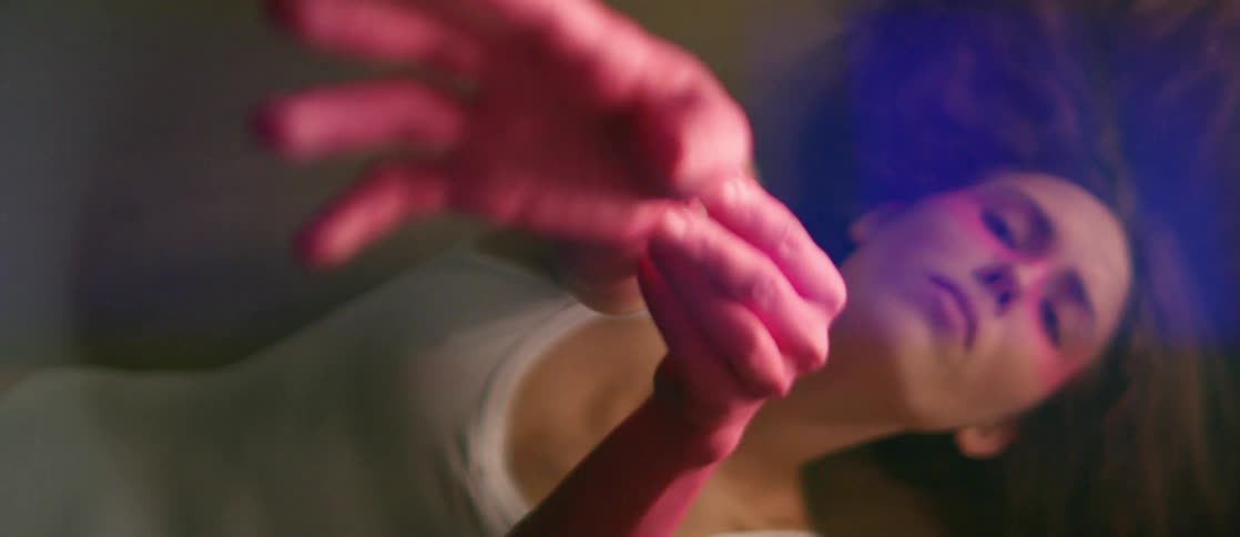 A woman holds her hands out in an abstract dance routine as she lays on the floor