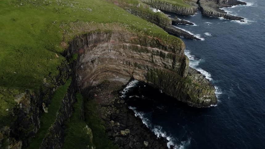 Waves crash around the base of a huge grass covered plateau