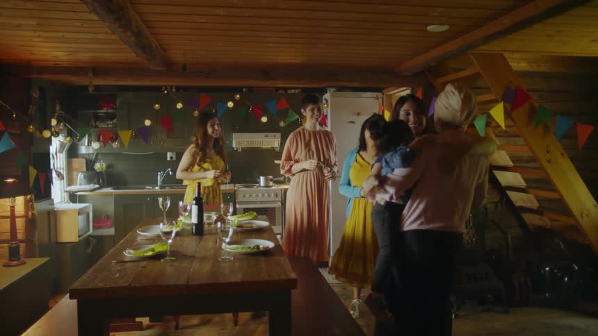 A woman carries a baby into a room where four people are waiting to celebrate a party