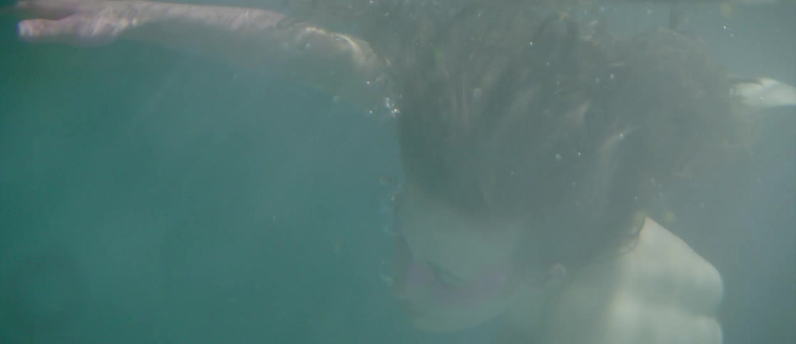 A woman swimming around underwater blowing bubbles