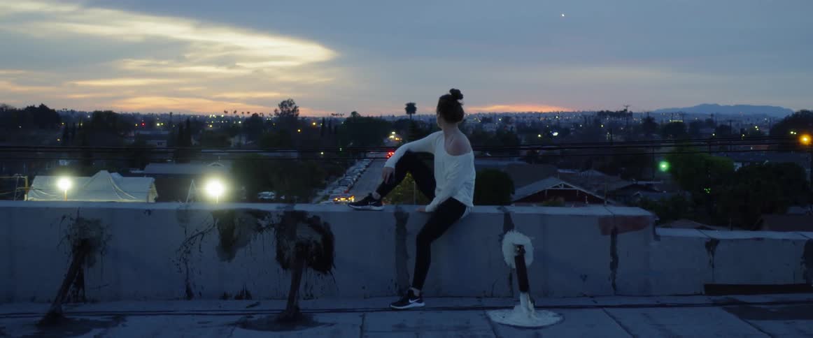 A woman sits on the ledge of a building rooftop