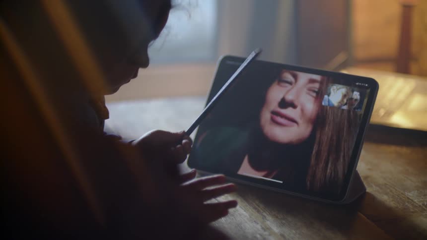 A woman is talking to a child via a video call inside in daylight