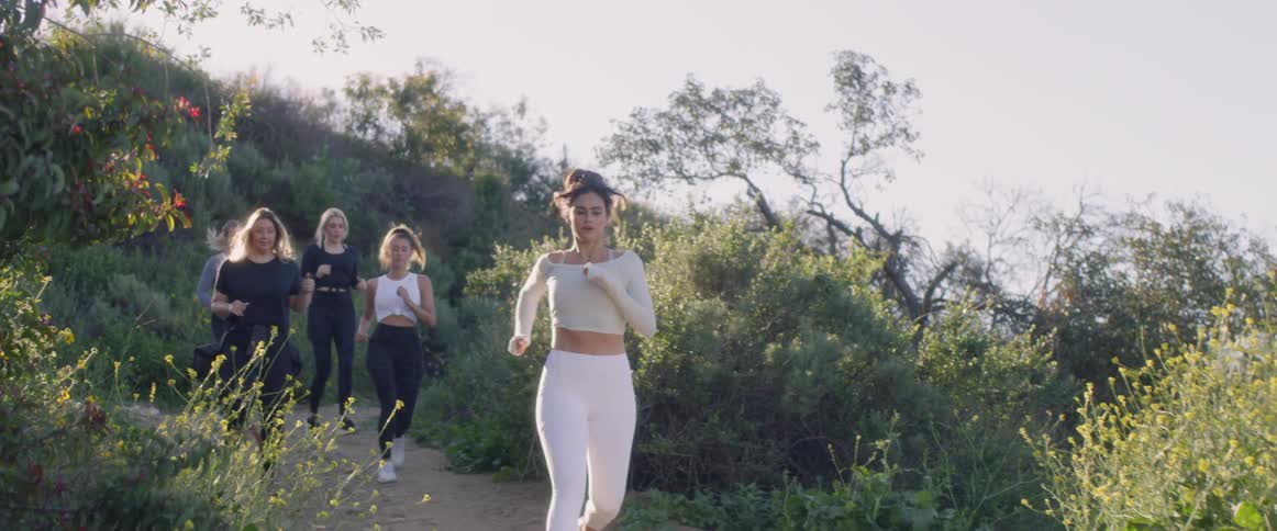Five women jog along a path lined with shrubs and wildflowers