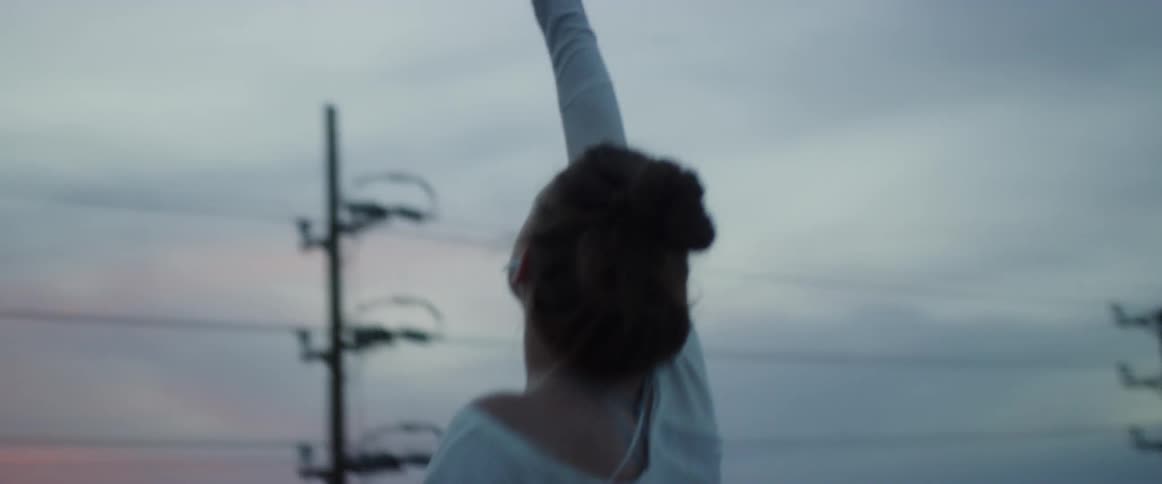A woman wearing earfuls raises up from a bent over position and reaches toward the sky