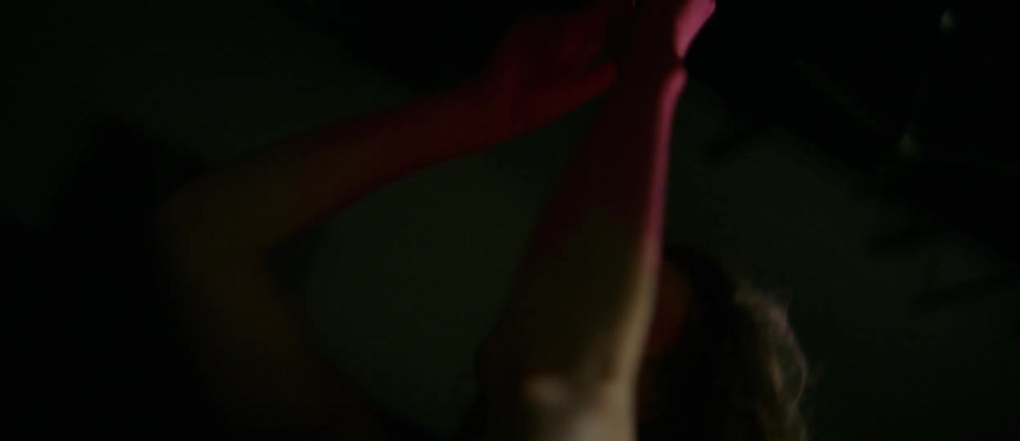 A woman with her forearms and hands painted pink does an interpretive dance in a room with flashing lights,