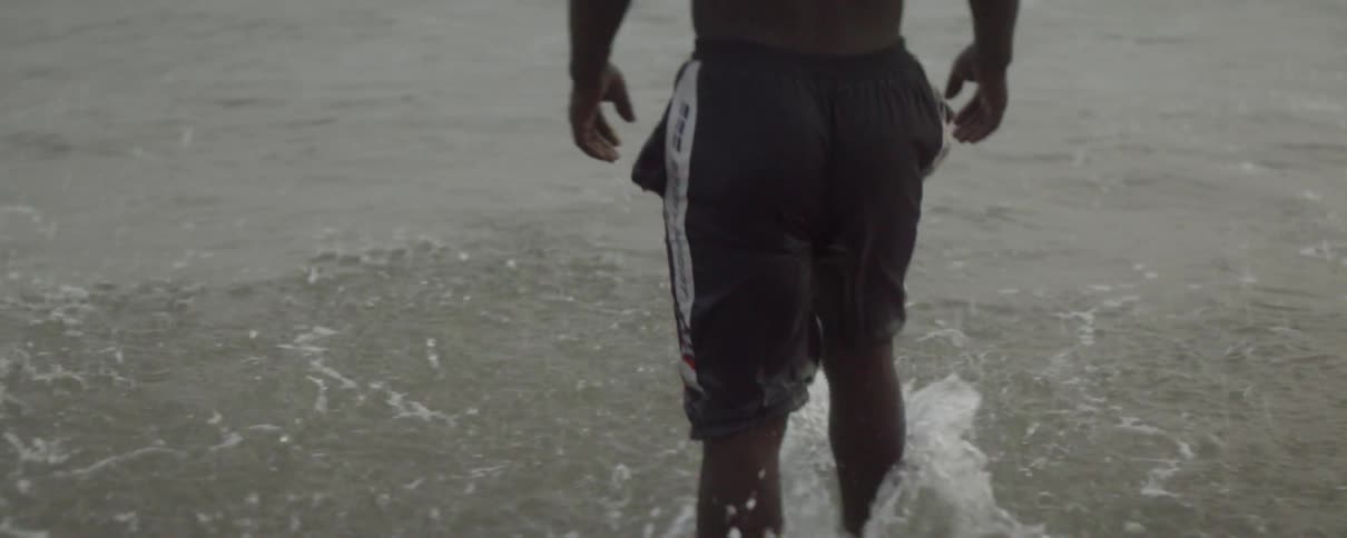 A man stands ankle deep in the ocean as he splashes through the waves flowing onto the beach