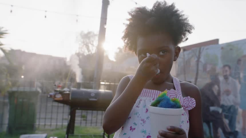 A young girl eating a snow cone next to a grill