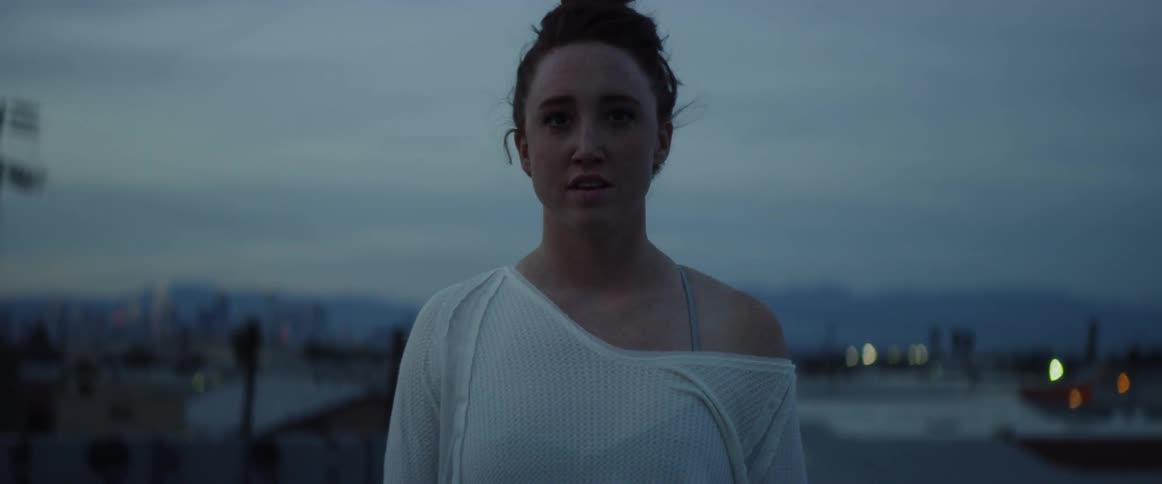 A woman in a white shirt stands on a rooftop at dusk