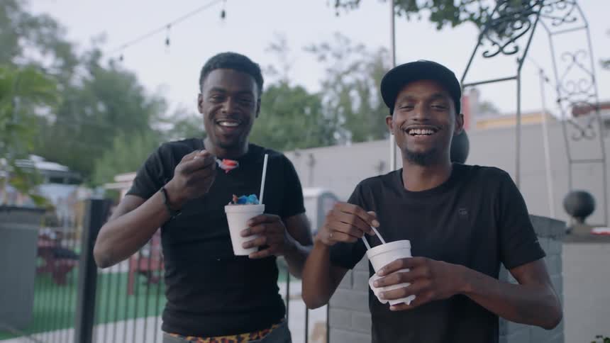 Two men smile as they happily eat colorful shaved ice