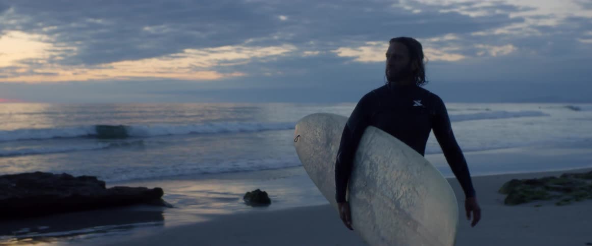 Man walking away from the sea on a beach while holding his surfboard