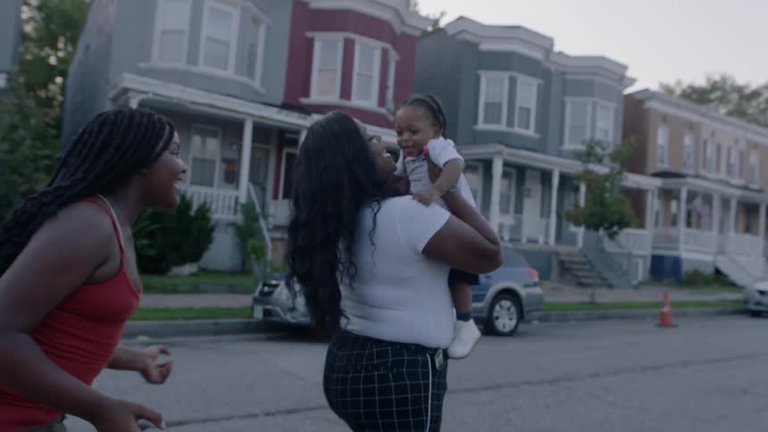 A woman makes a baby laugh by bouncing them in the air as another woman follows