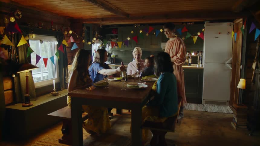 A group of people sit around a table in a kitchen talking and smiling