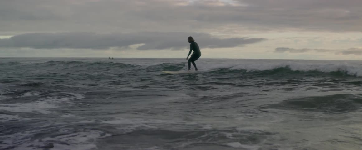 Surfer in a wetsuit rides a small wave to the shore