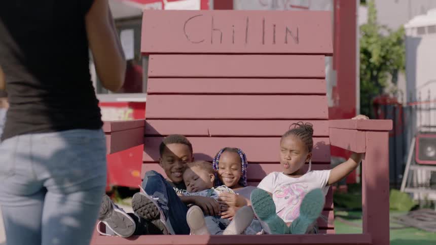 A woman taking a photo of four children sitting in a big chair