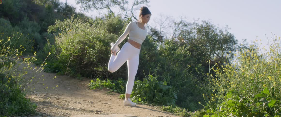 A jogger dressed in white exercise clothes stretches on a hill