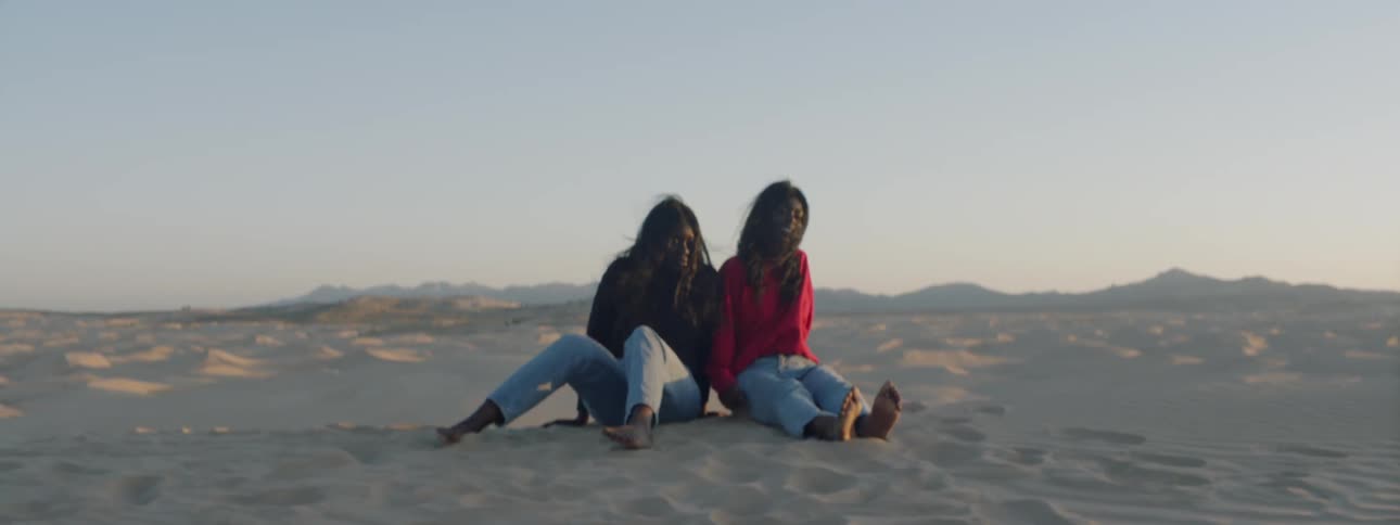 Two women sit in the sandy desert on a sunny day