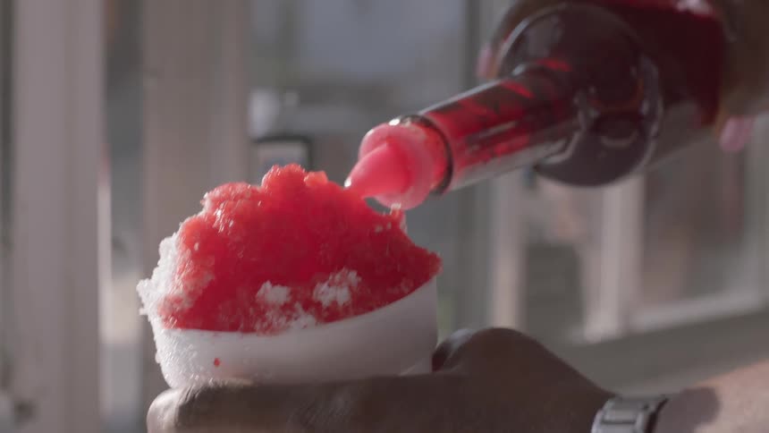 A man puts red syrup on shaved ice