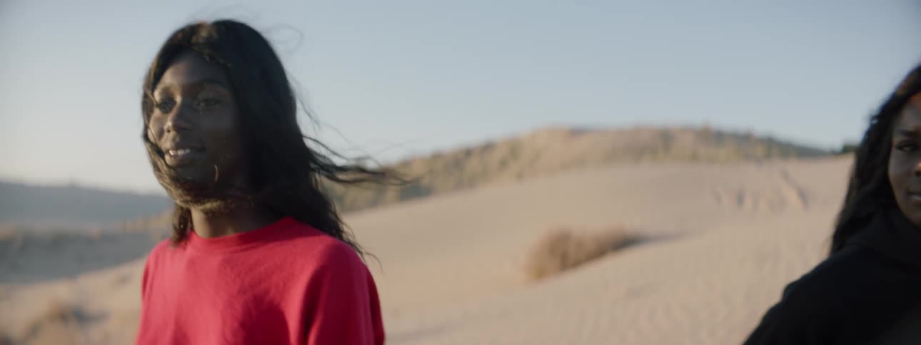 Two women look at each other and smile as they stand on sand