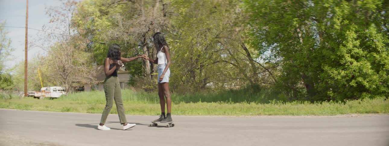 A woman holding a video camera pulls another woman down the street on a skateboard