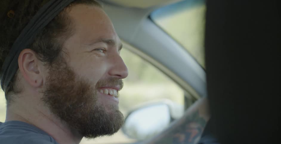 A man smiles as he drives and looks over to the passenger in the seat next to him