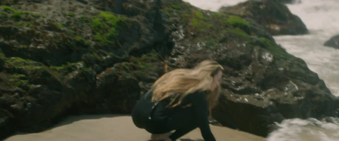 A woman that is standing on some rocks next to the shore and rubbing water on her face