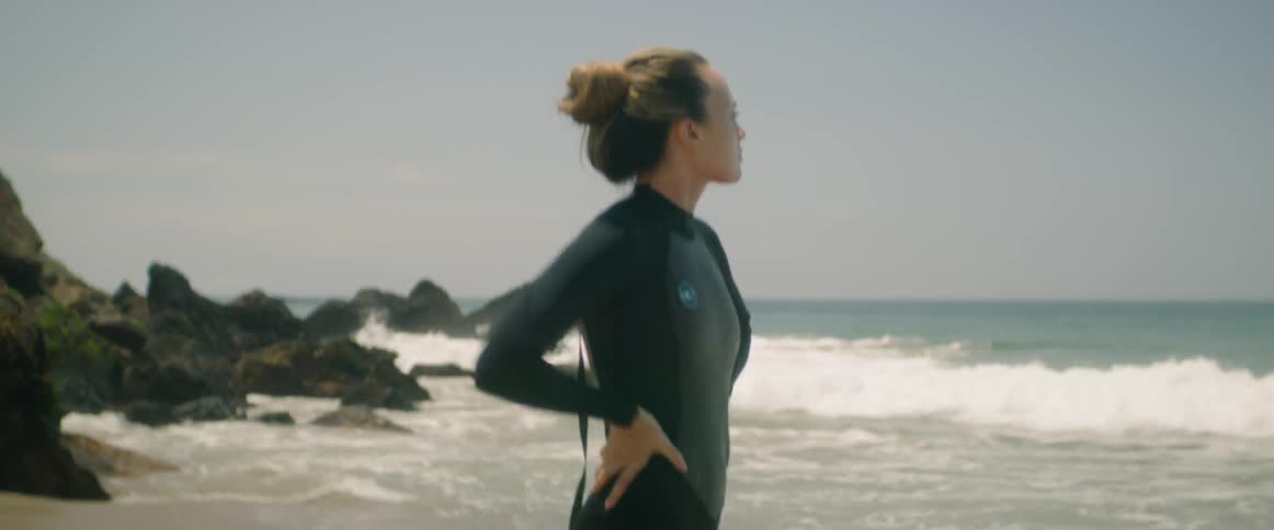 A woman in a wet suit standing at the edge of the ocean