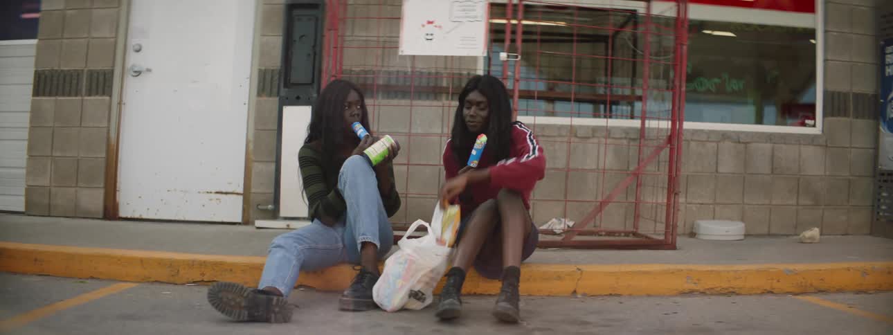Two young women sit down outside of a shop to eat