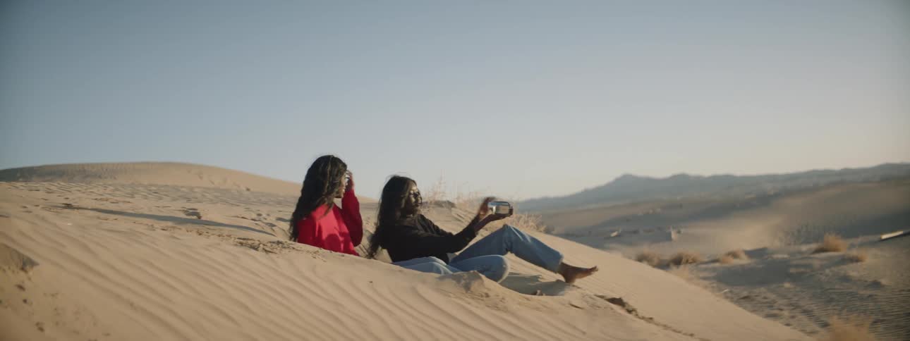 Two women record a video of themselves on a sand dune in the desert