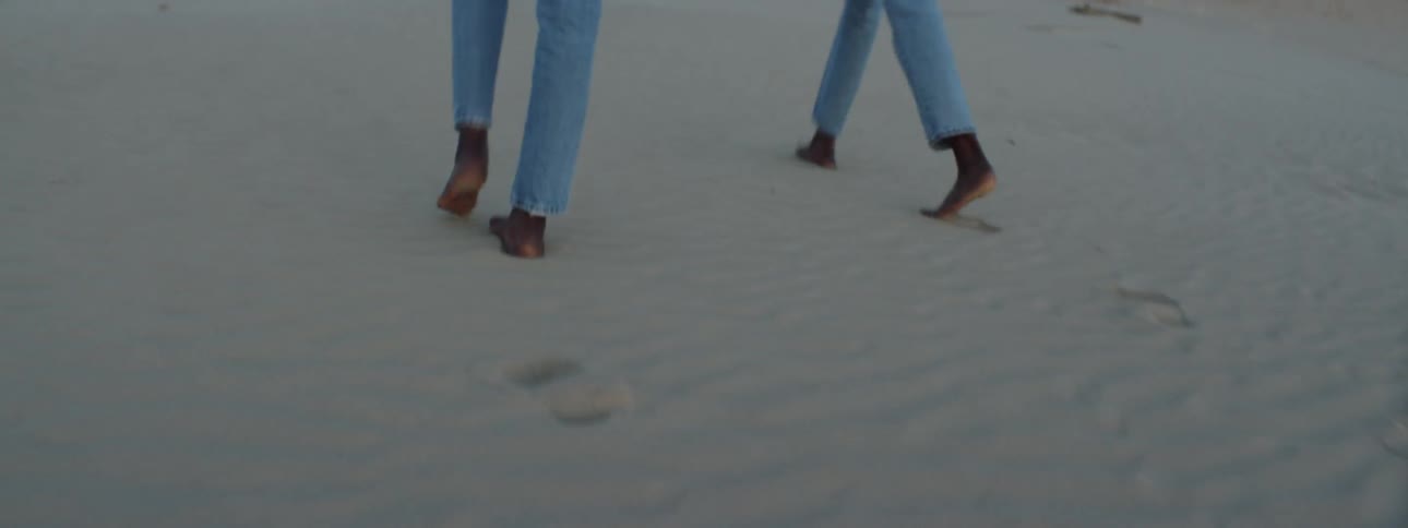 Two people walk barefoot through the desert sand