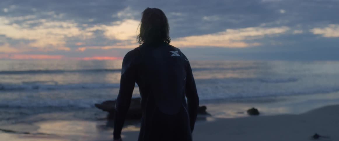 A man lays his surfboard down as he looks out at the ocean