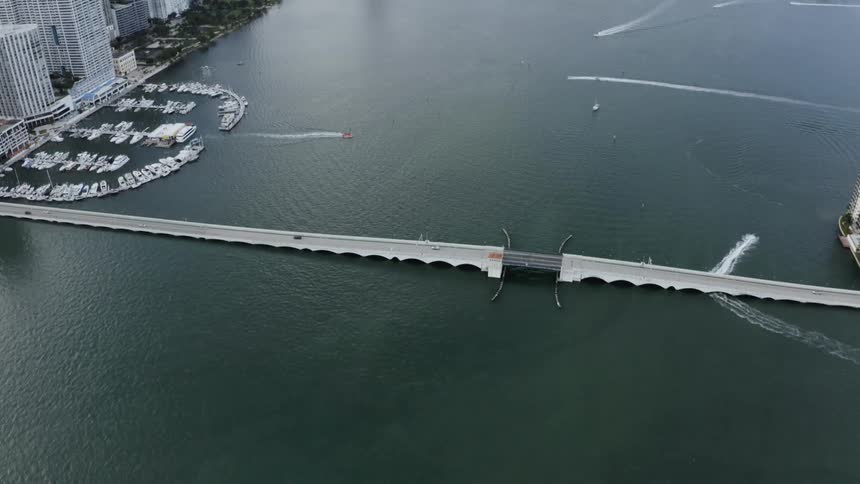 Vehicles drive over a bridge while boats float on the water