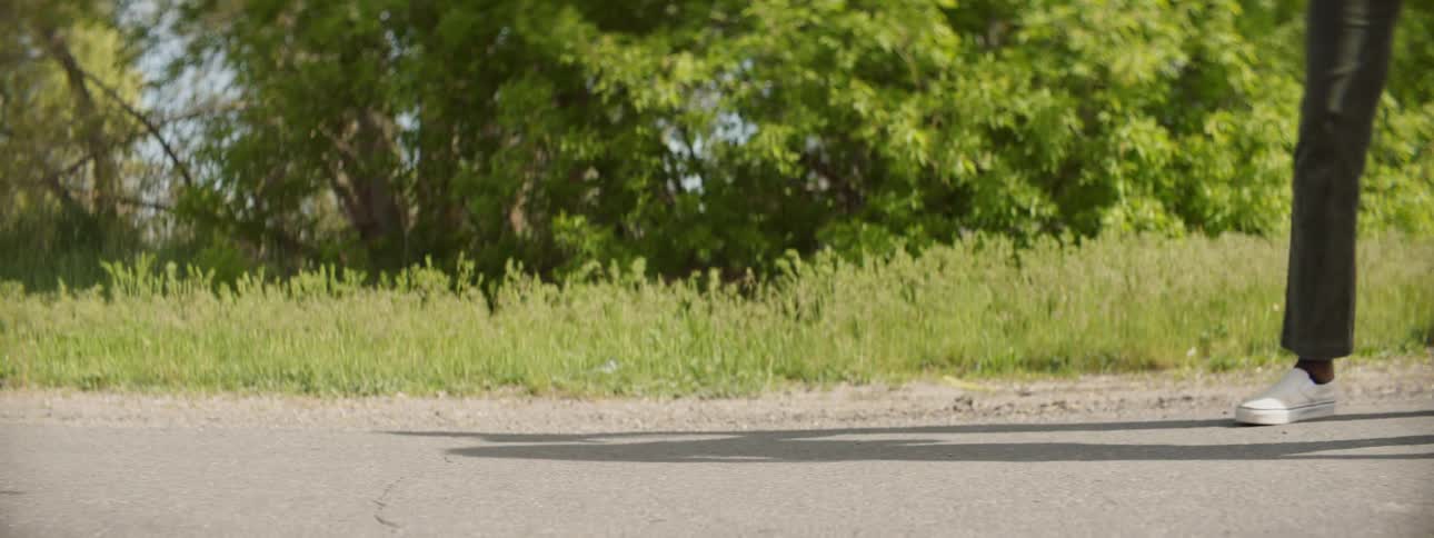 Person rides on a skateboard and another person walks on a sunny country road
