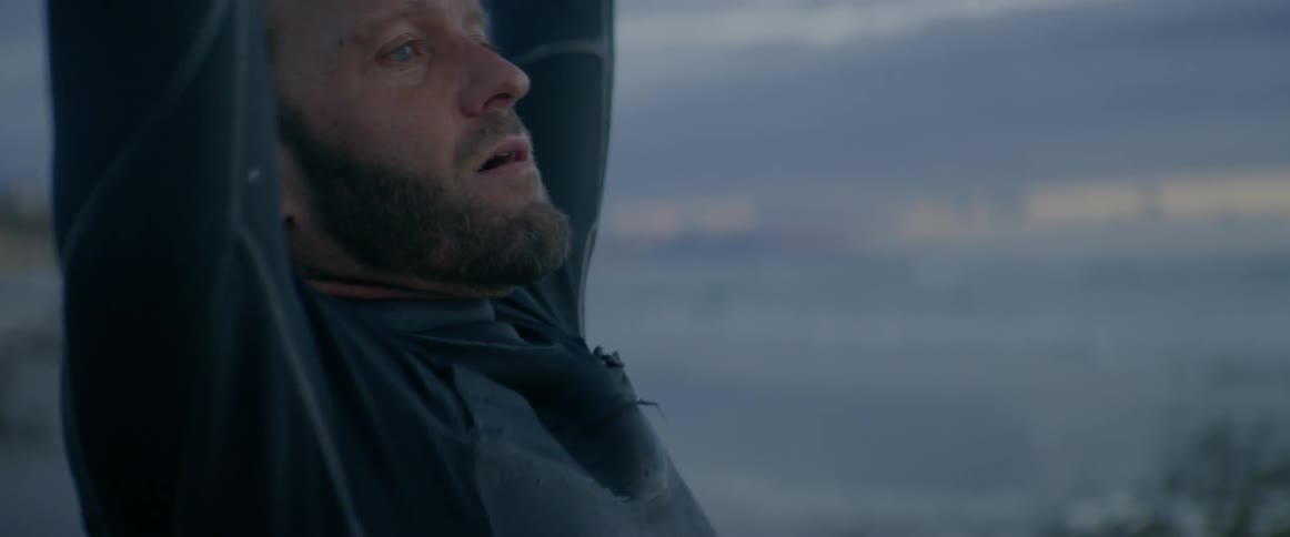 A man in a wet suit stretches on a beach at sunset