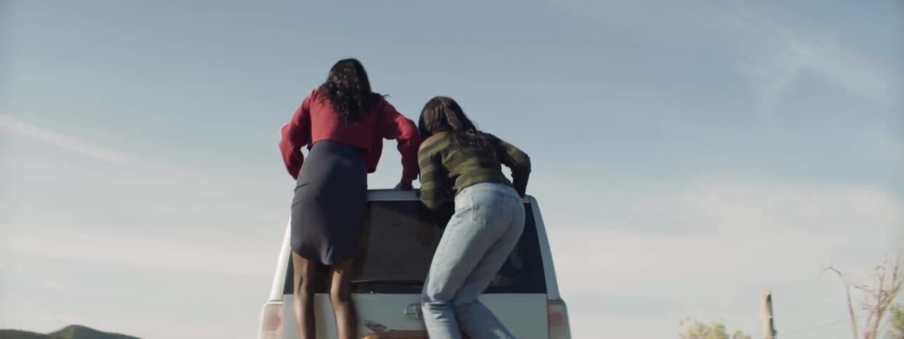 Two woman jump to sit on the roof of a vehicle
