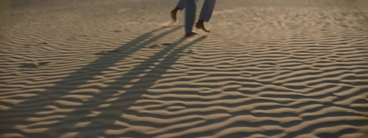 Two women walk barefoot through a desert