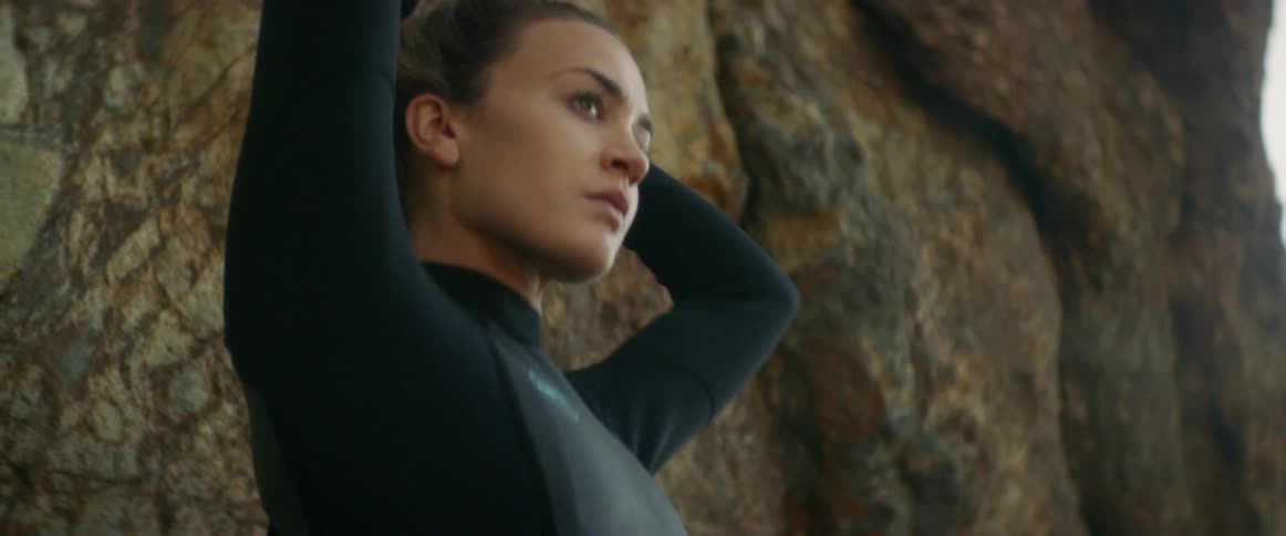 A woman in a wet suit fixes her hair into a bun