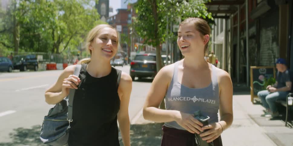 Two women walk along the sidewalk by a busy road in a city