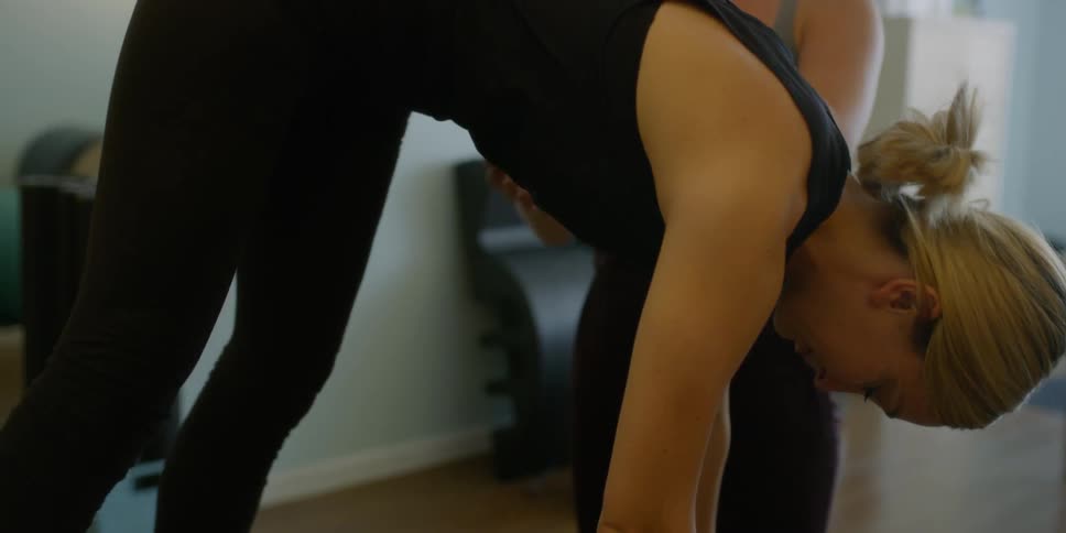 A woman helps another woman with her exercises in a well lit room
