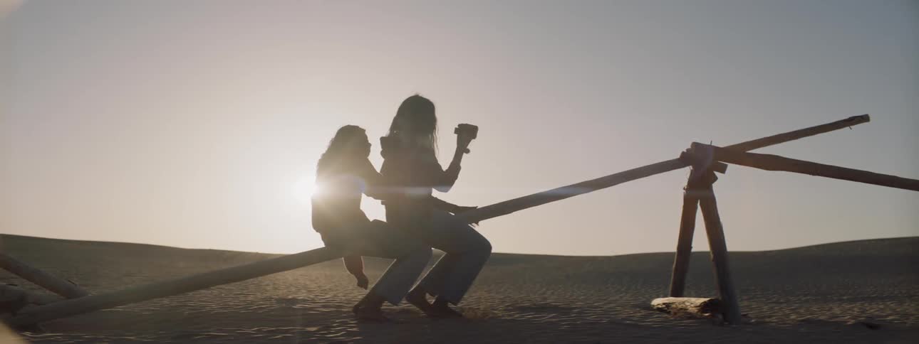 Two women sit and bounce on a pole in the desert