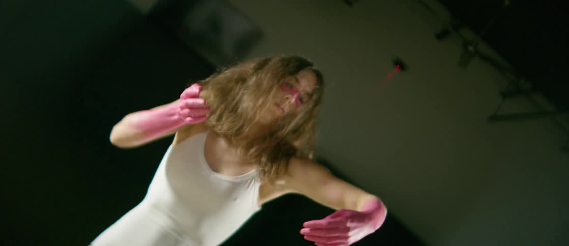 A woman with her forearms and hands painted pink does an interpretive dance in a spotlight