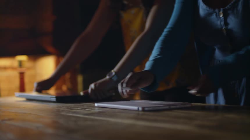 Two women in a dark room place laptops on a table