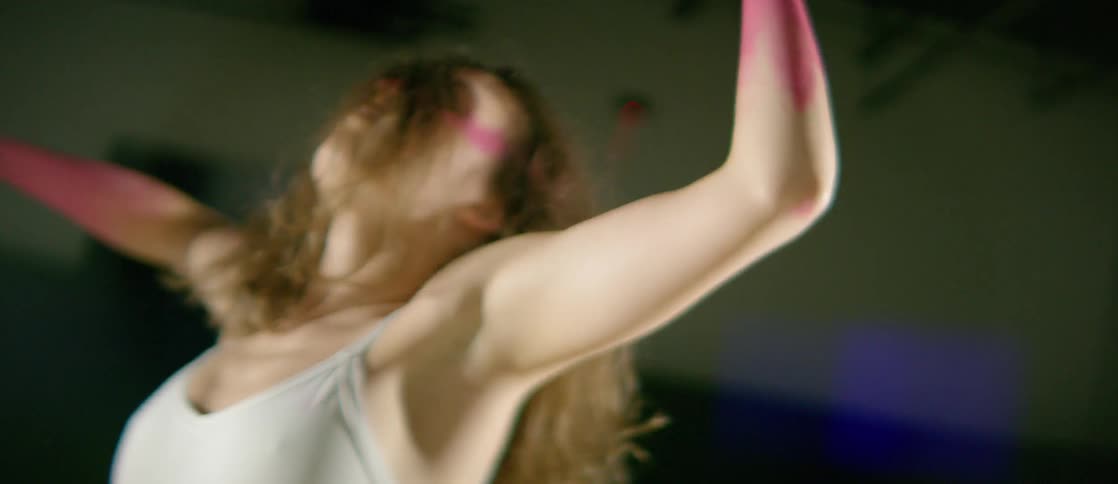 A woman with her forearms and hands painted pink does an interpretive dance in a spotlight
