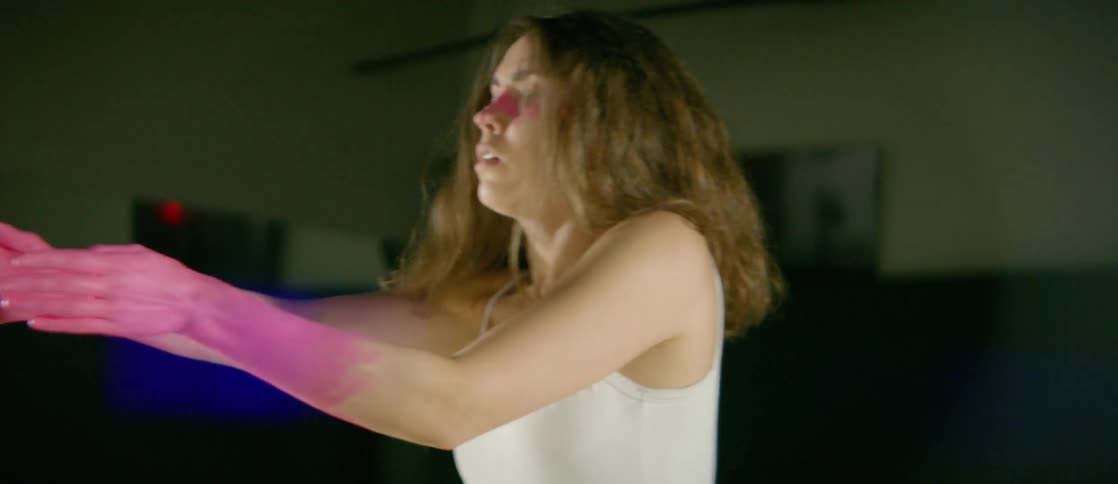 A woman with splatters of pink body makeup, dances in a studio