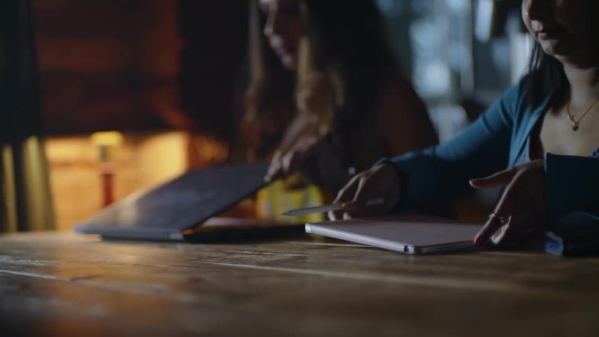 Two women sit on table and open laptops