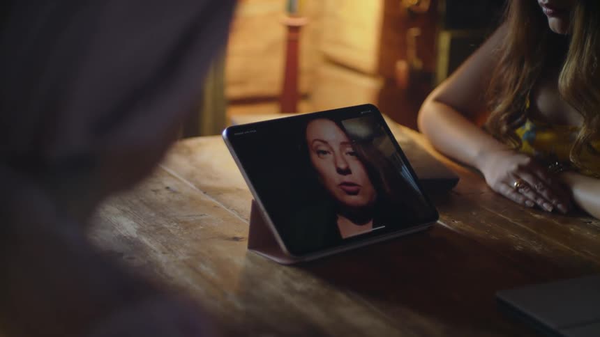 Multiple people surround a table with a tablet streaming a video call