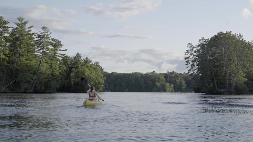 Woman paddles a yellow kayak in a lake