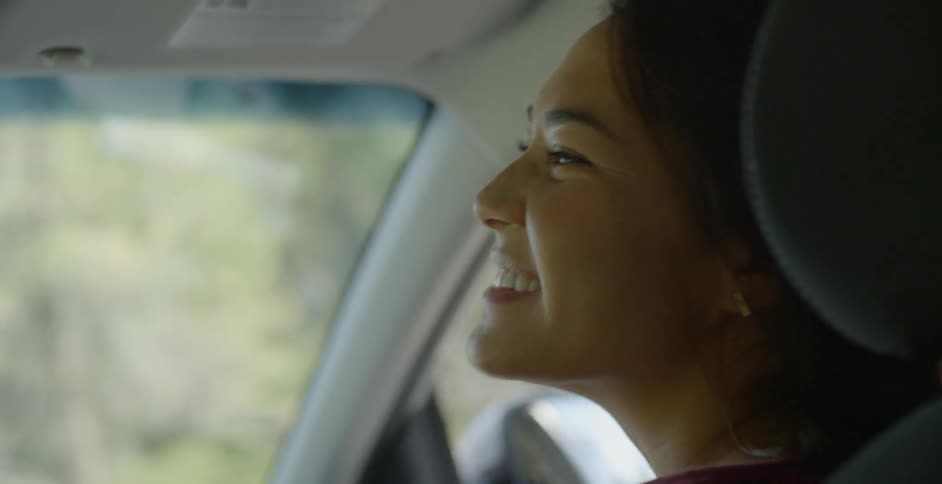A woman is smiling and turning to look at the driver as she rides in a car in daylight