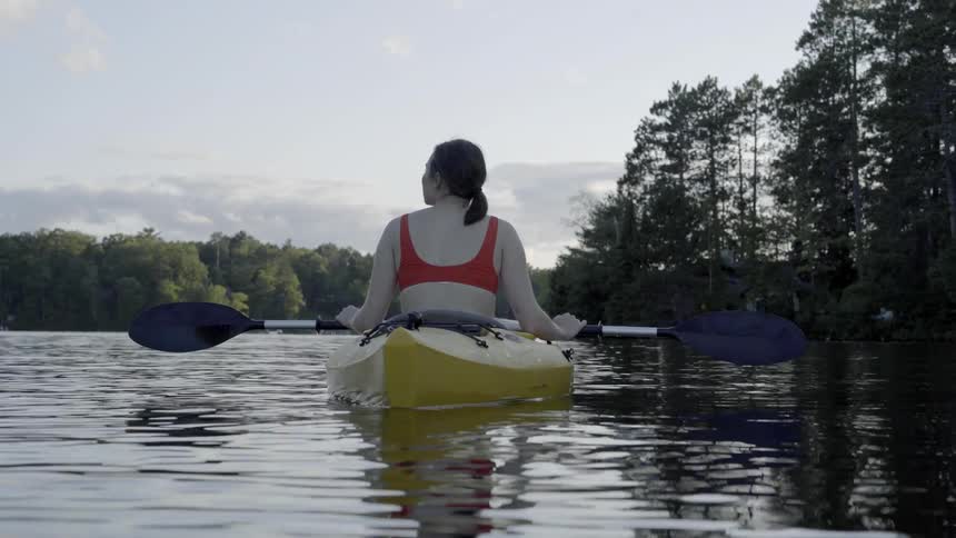 A woman sits in a canoe on a river lined with trees