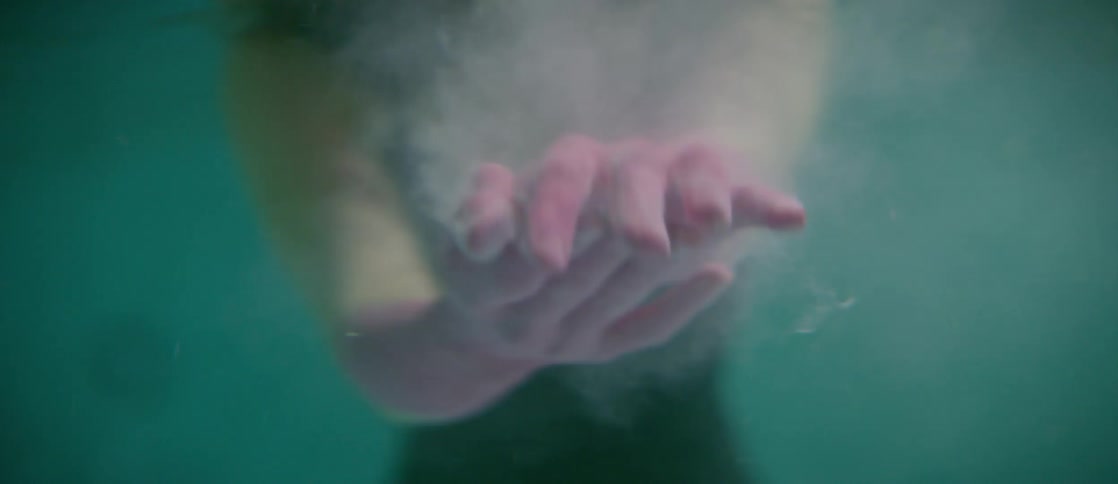 A woman with her forearms and hands painted pink washes the paint from her hands underwater