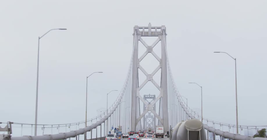 A bunch of cars and trucks drive along a large bridge